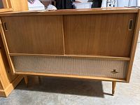 Full front view of the mid-century modern wooden stereo cabinet with speaker grille and tapered legs.