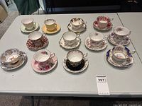 Full overhead view of all 10 porcelain teacups and matching saucers arranged on a table, showing diverse floral designs and gold trims.