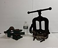 Two vintage vises side by side with a water bottle for size reference on a white background