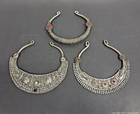 Top view of three vintage ethnic tribal torque necklaces arranged on black background showing front sides with adornments and varied designs