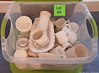 Top view of a plastic bin filled with various white milk glass and ceramic dishes including mugs, bowls, trays, and a ladle.