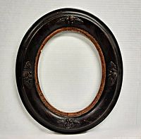 Front view of antique oval wooden frame showing dark finish and hand-carved floral and nut motifs at the edges.