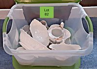 Top-down view of plastic bin containing various white ceramic dishes including oval serving plates, small bowls, and a creamer with gold trim.