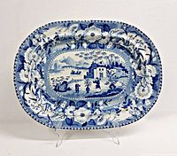 Photo of large antique blue and white transferware platter on stand showing front oval scene and floral bird border