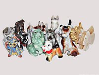 Front view of all 14 dog figurines arranged in a group on a flat surface, showing different materials, colors and sizes.