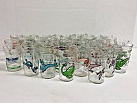Full lot of 43 Welch's jelly glasses arranged in rows showing various cartoon and dinosaur designs.