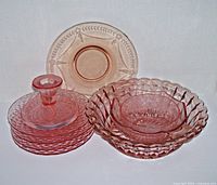 Set of pink Depression era glassware including bowls, candle holder, and plates arranged on white background.