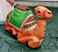 Close-up photo of the camel blow mold showing detailed paint, green draped cloth, and red harness.