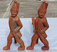 Front view of two cast iron Hessian soldier andirons showing detailed soldier figures with hats, coats, and boots in rusty condition.