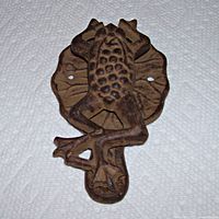 Front-angle view of vintage cast metal frog door knocker showing the frog on a textured lily pad with two mounting holes.