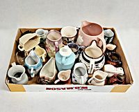 Top view of the 23 assorted vintage creamers and small pitchers arranged closely together in a cardboard box, showing a variety of colors, shapes, and materials including ceramic and glass.