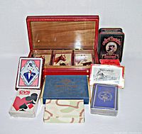 View of the 9 vintage playing card decks arranged around a red lidded box showing various card themes and packaging.