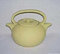 Front view of the vintage yellow ceramic twin spout teapot with lid on.