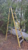 Full view of yellow fiberglass A-frame ladder standing outdoors