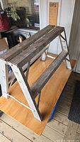 Side angle of the aluminum 2-step stool on a wooden surface, showing its structure and wear.