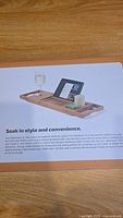 Photo of the bamboo bathtub caddy tray box with image showing wine glass, tablet, and candle holders.