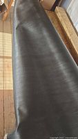Close-up photo showing black vinyl fabric partially unrolled, displaying texture and width.