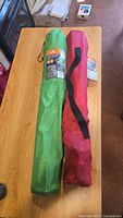 Two camp chairs in their carrying bags, one green and one red, on a wooden table.