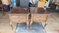 Two matching Queen Anne style end tables showing the full front and top view, highlighting the wood finish, brass drawer handles, and cabriole legs.