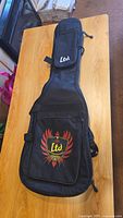 Black nylon LTD guitar case backpack with large zippered front pocket and flat laid on wood table.