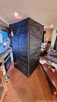 Black portable grow tent fully assembled in living room environment