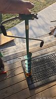 Photo of green manual ice fishing auger showing spiral blade and handle on wooden steps.