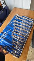 Full view of entire 14-piece Gray SAE wrench set in blue roll-up pouch laid on wooden table.