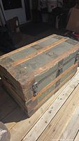 View of the old steamer trunk from the top and side showing wooden reinforced slats, metal latches, and overall aged condition.