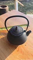 Side view of the small black cast iron teapot on a wooden table with measuring tape showing length of about 5.5 inches.