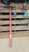 Full length view of the red adjustable jack post on wooden steps, showing overall shape and size. Includes a can and container nearby for scale.