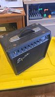 Right front angle view of the black Fender Squier Champ 15GR amplifier with multiple control knobs and Squier logo.