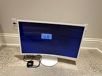 White 32-inch curved Samsung monitor with cables, turned on showing 'Check Signal Cable' message on screen.