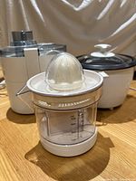Three Hamilton Beach appliances shown together: juice extractor, citrus juicer in front, and mini rice cooker with lid in back.