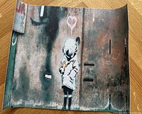 Rolled canvas print of Banksy Space Girl artwork laid flat on wood surface.