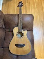 Full front view of the natural finish right-handed BeaverCreek travel size steel string guitar laid on brown surface.