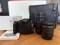 Camera body, two lenses, box, bag, and manuals arranged on table
