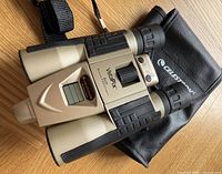 Top view showing the binoculars with LCD screen, controls, and carrying strap beside the Celestron branded black soft case.