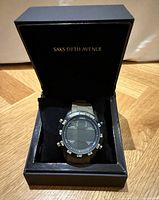 Blue digital sports watch with black round face and digital display in a black Saks Fifth Avenue box.