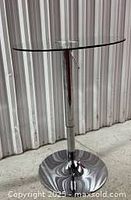 Side view of glass bar table showing clear round glass top and chrome steel column base with adjustable height mechanism.