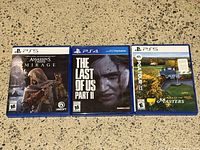 Front view of 3 game cases: Assassin's Creed Mirage (PS5), The Last of Us Part II (PS4), Road to the Masters PGA Tour Golf (PS5)