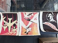 Photo showing 3 canvas propaganda posters laid side by side, featuring US Air Force bombers, white doves, and a woman soldier with Vietnamese text