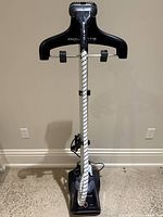 Front view of the Rowenta standing fabric steamer showing the base, telescopic pole, and steam hose.