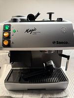 Front view of silver Saeco Magic Cappuccino Combi machine with illuminated buttons and portafilter in drip tray
