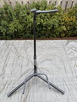 Black Silvertone guitar stand assembled on outdoor tarp, showing full stand with padded neck support and tripod base.