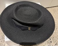 Top angled view showing the round crown and woven texture of the black boater hat.