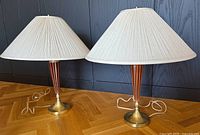 Pair of vintage mid century modern table lamps side by side. Lamps have brass bases, wood column accents, and large pleated pale fabric lampshades.