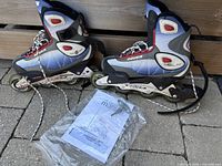 Side angle of Bauer women's rollerblades in blue, black, white and red, showing four wheels each and attached laces. Hex key and manual included in front.