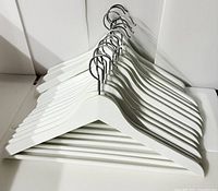 Fifteen white wooden hangers stacked together showing full set.