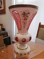 Front angle showing pink glass panels with scroll pattern, hand painted floral decorations, and gold trim on white milk glass body.
