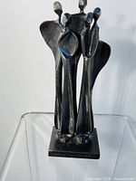 Front view of the steel sculpture showing four abstract figures and the rectangular base with signature and stamping.